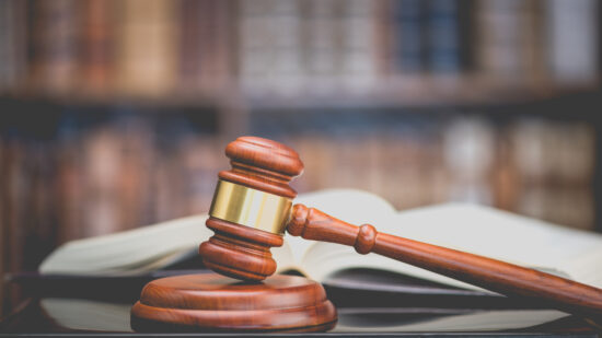 Legal office of lawyers, justice and law concept : Judge's gavel or hammer and base used by a judge person on a desk in a courtroom with blurred books and a bookshelf or bookcase in the background.