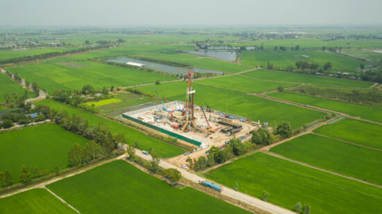 Oil and gas land drilling rig onshore in the middle of a rice field aerial view from a drone